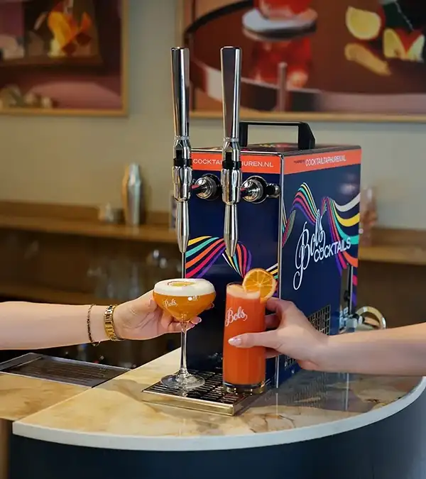 Twee handen die cocktails vasthouden voor een blauwe cocktailtap met het logo van Bols Cocktails. De cocktails zijn oranje en gegarneerd met een schijfje sinaasappel